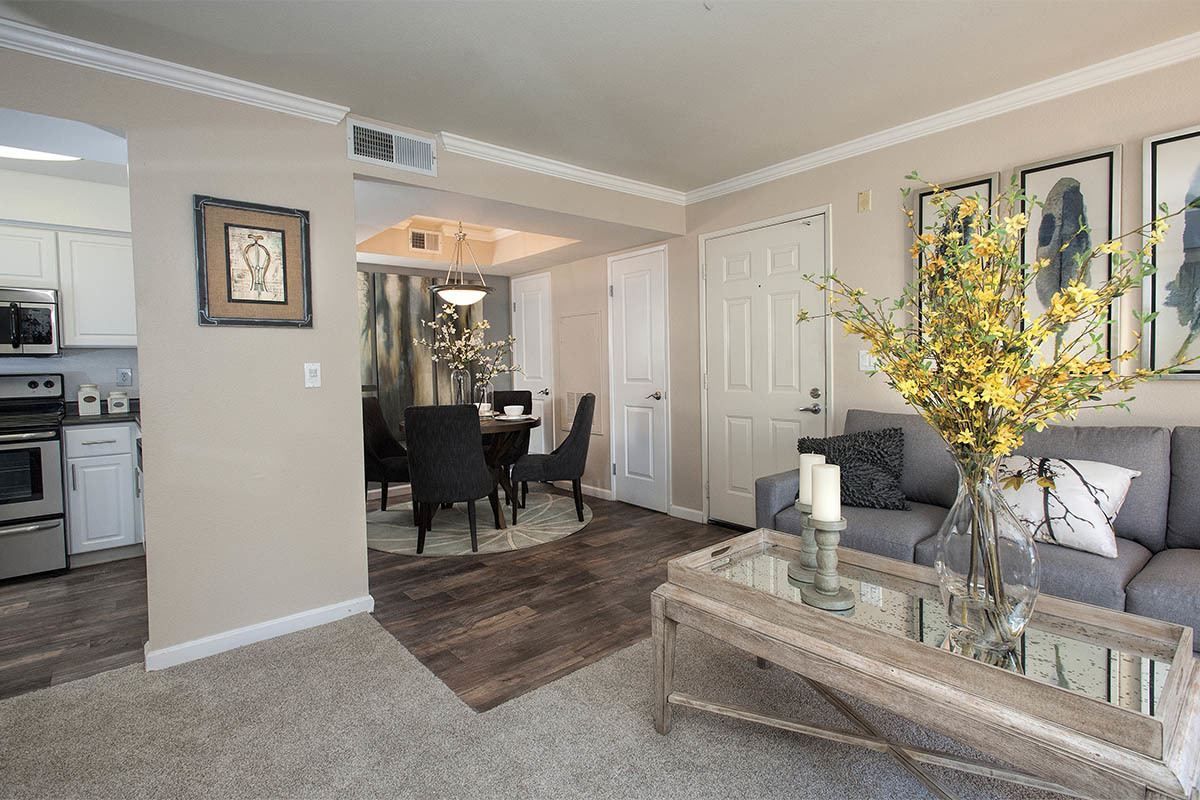 Open-concept living area with a gray sofa, glass coffee table, and dining table in an apartment.