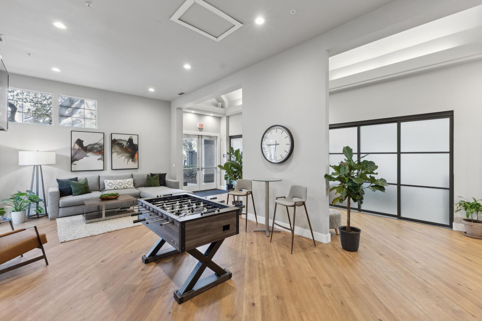 Interior community lounge with foosball table, sofa, plants, and frosted glass doors.