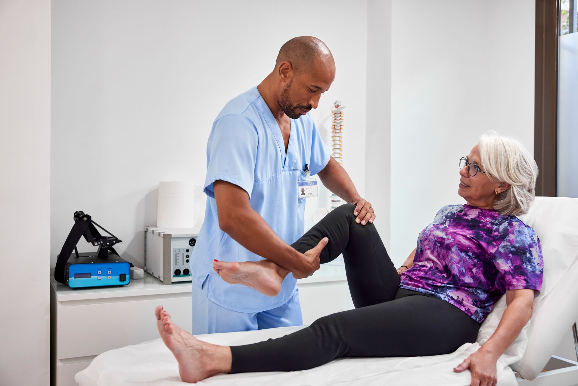 A chiropractor is stretching the leg of an elderly patient.