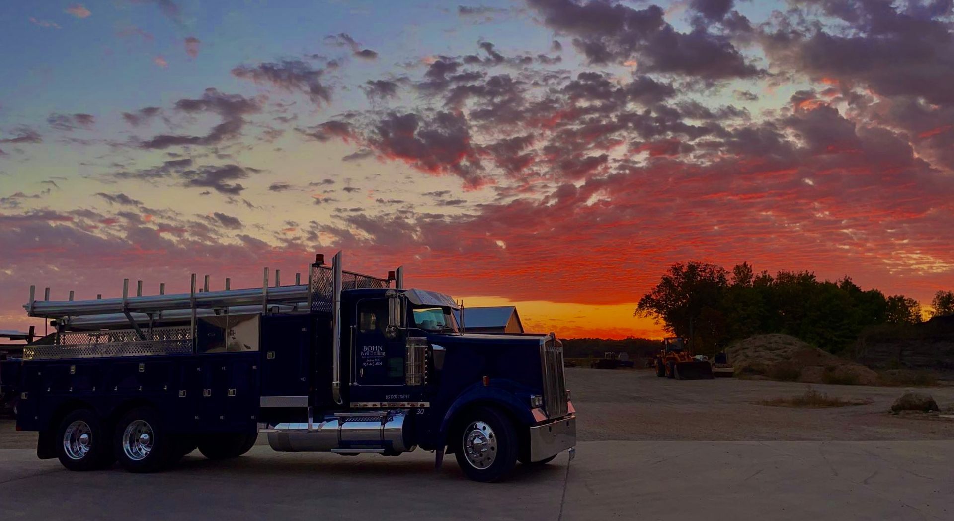 A blue semi truck is parked in a parking lot at sunset.