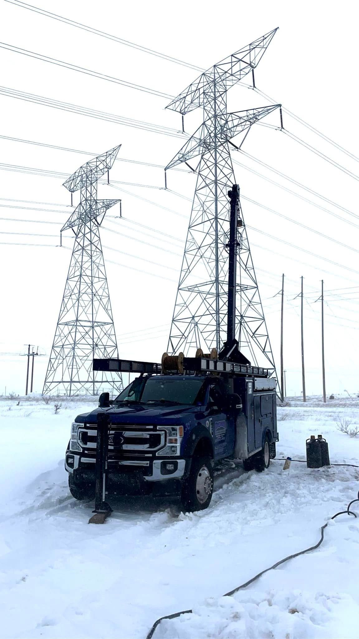 A truck is parked in the snow in front of power lines.