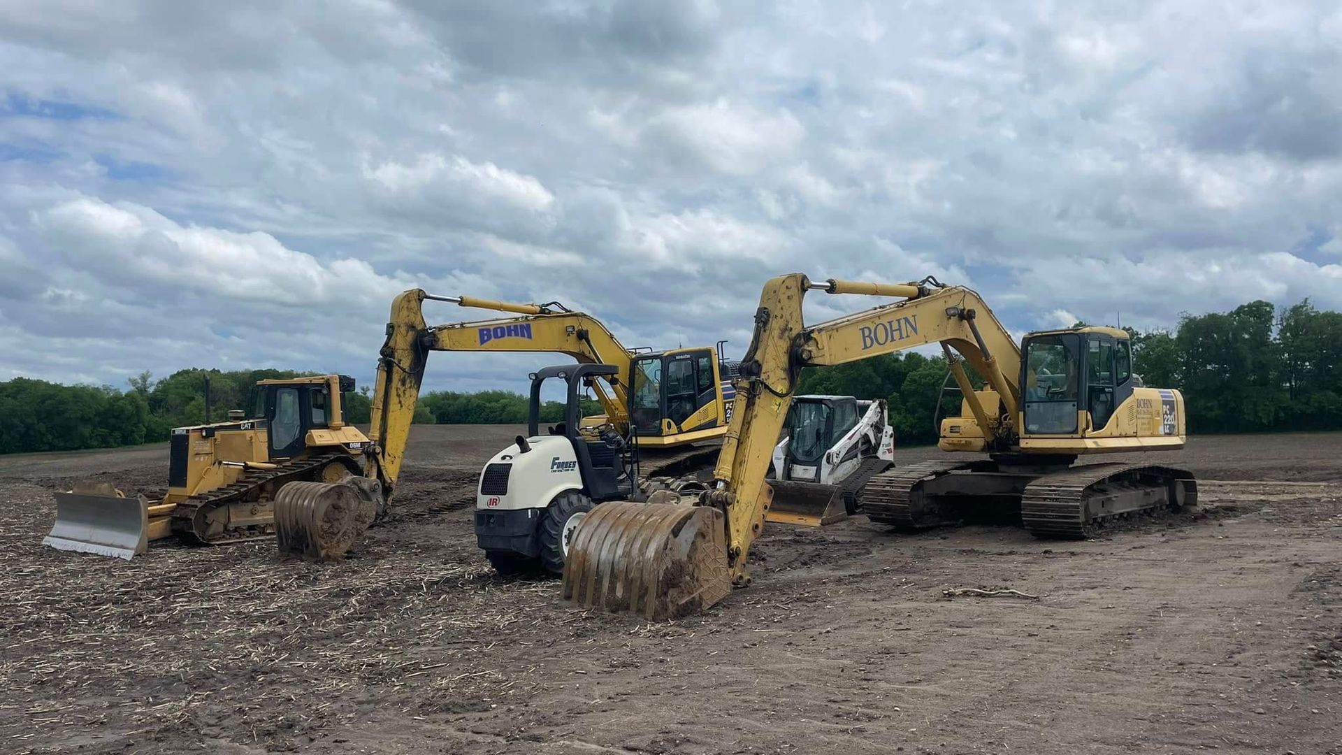 A group of construction vehicles are parked in a dirt field.