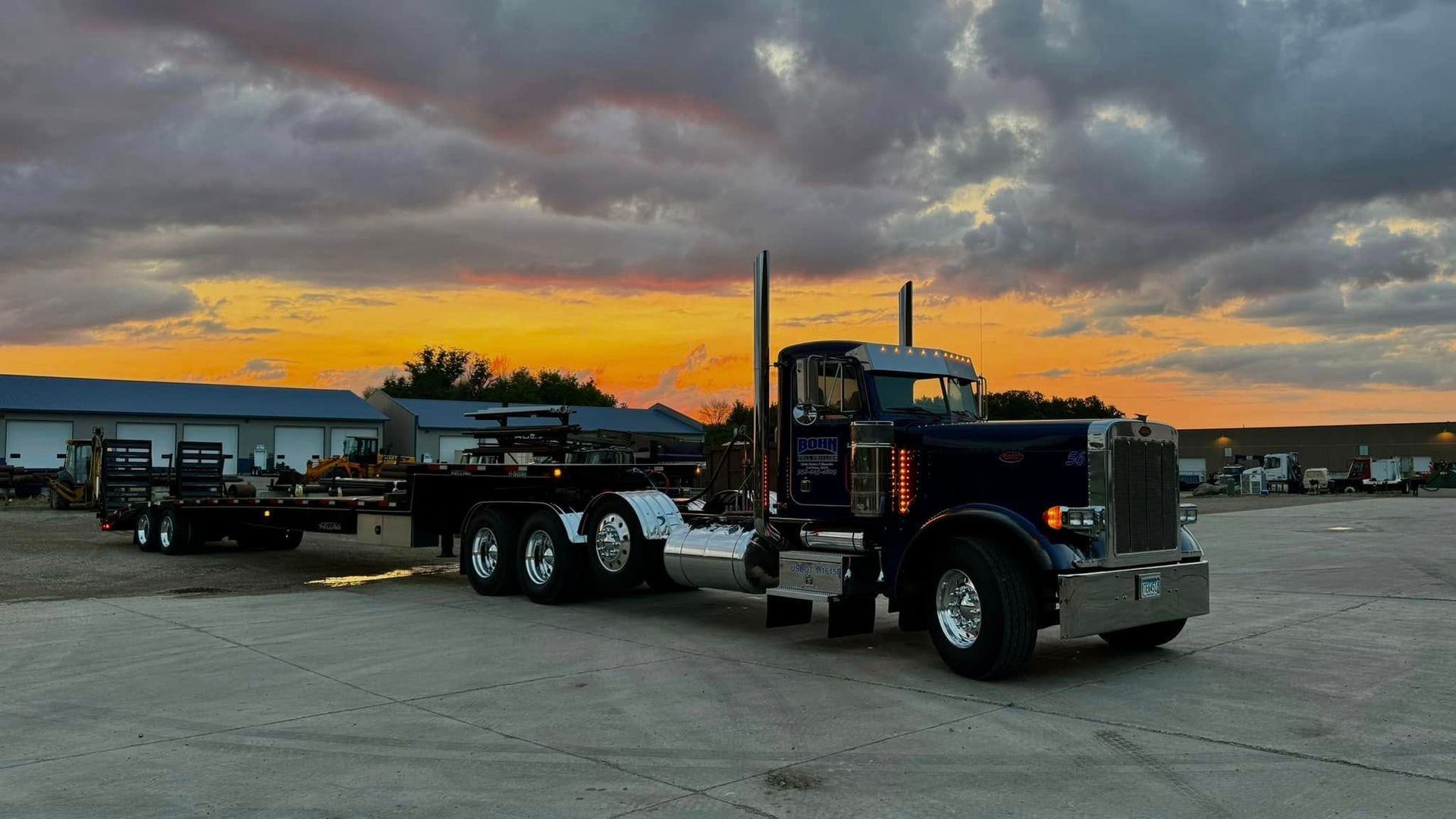 A semi truck is parked in a parking lot at sunset.
