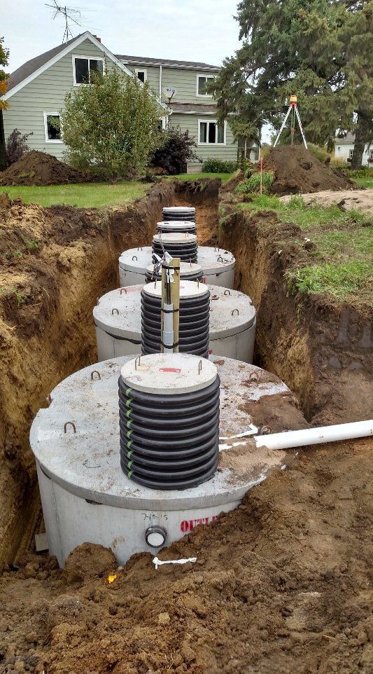 A row of septic tanks are sitting in the dirt in front of a house.