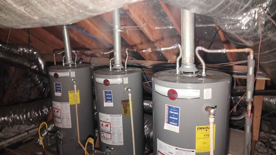Three water heaters are sitting in the attic of a house.