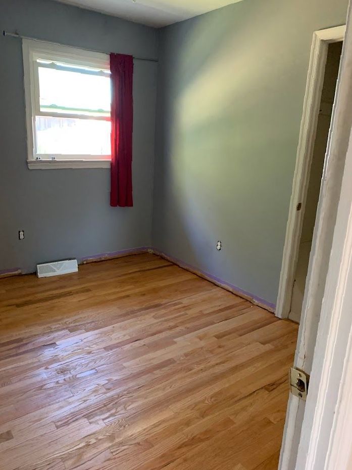 An empty bedroom with hardwood floors and a window.