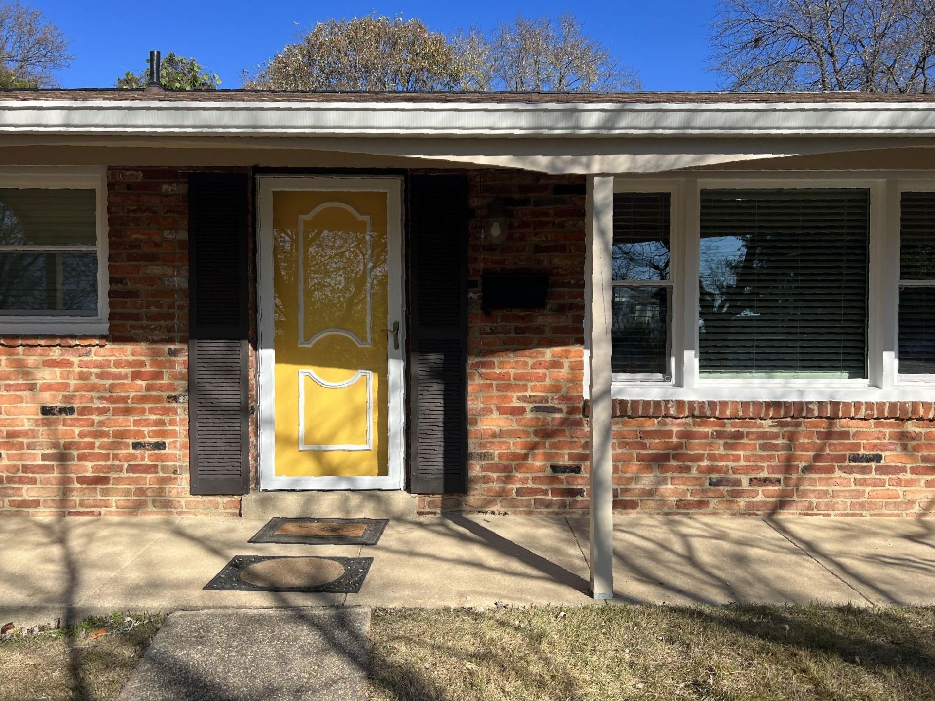 A brick house with a yellow door and black shutters.