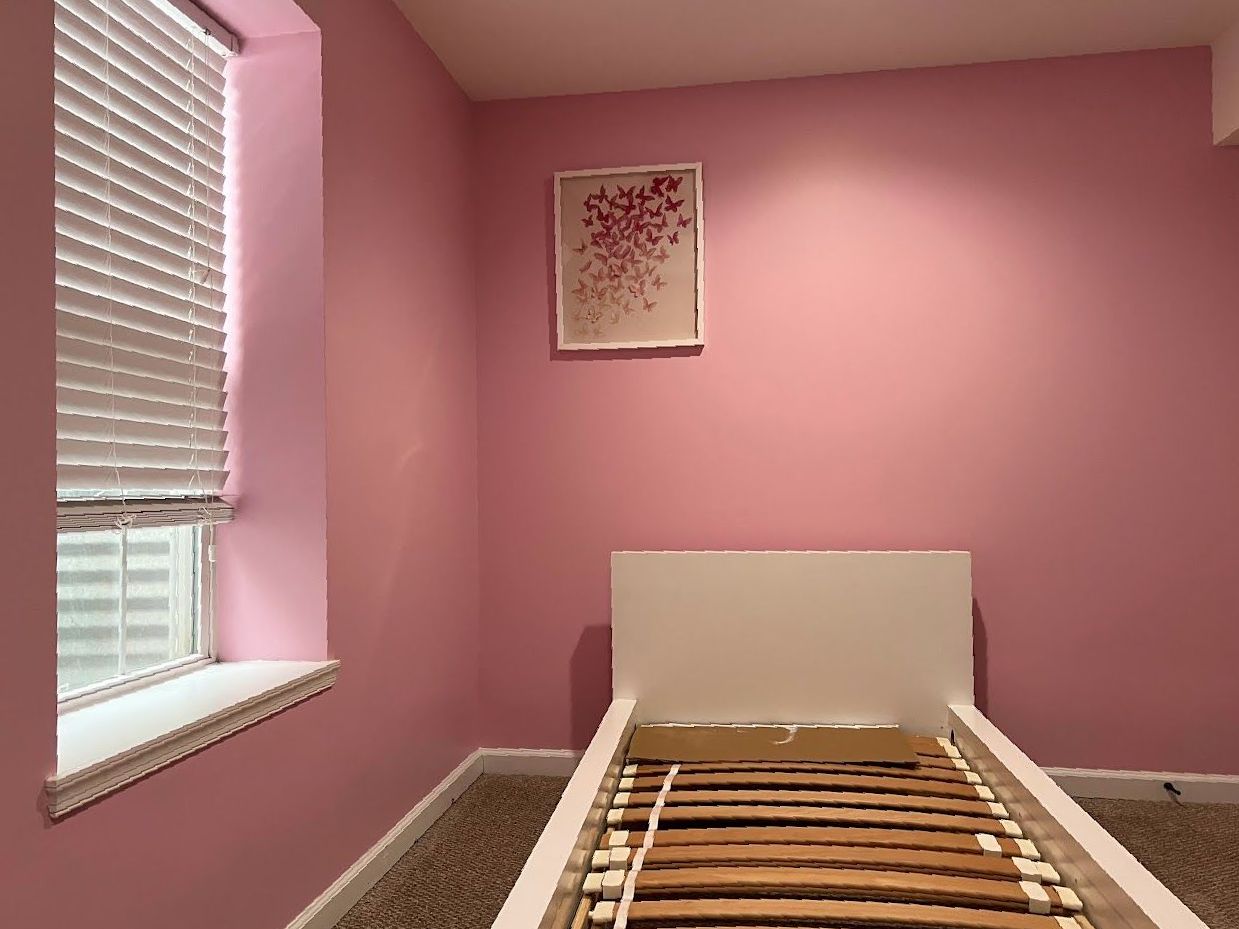 A bedroom with pink walls and a white bed