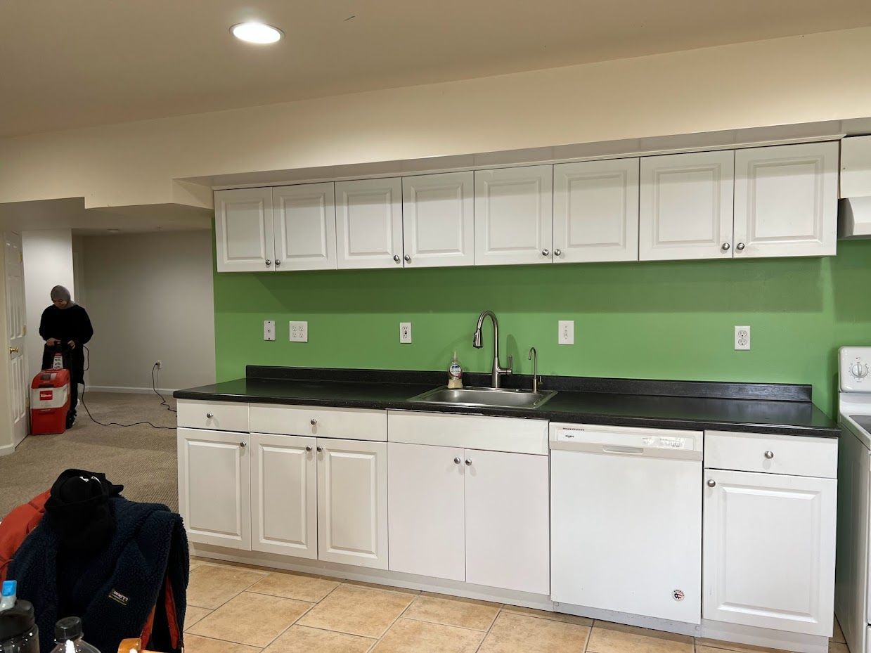 A kitchen with white cabinets , a sink , and a green wall.