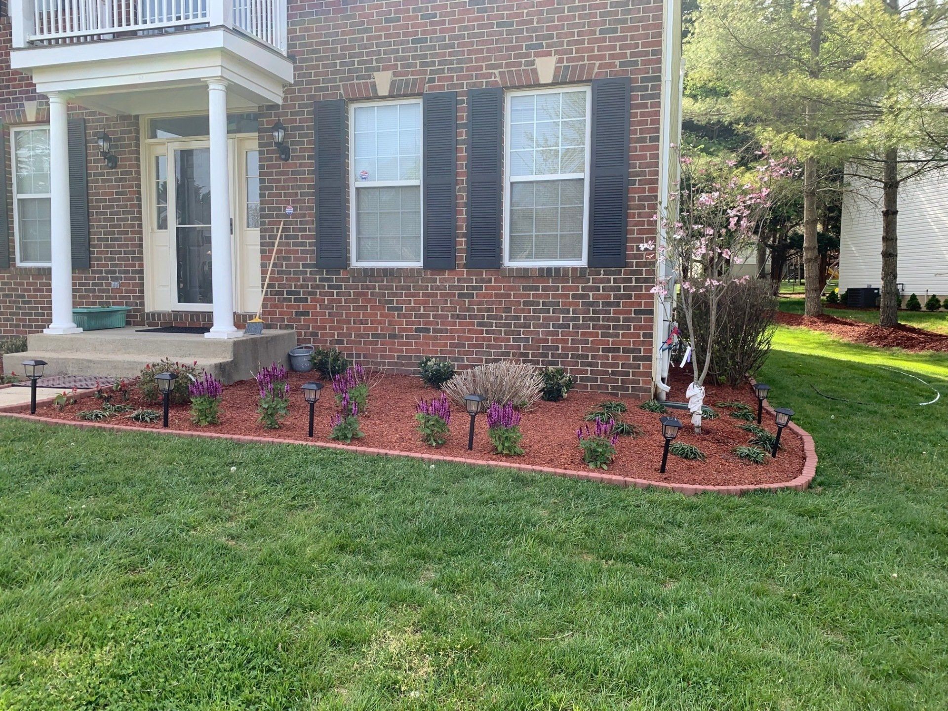 A brick house with a lush green lawn and flowers in front of it.