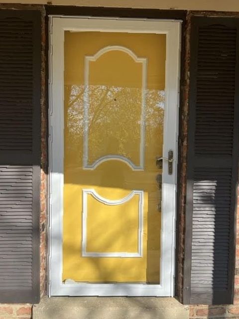 A yellow door with white trim and shutters on a brick building