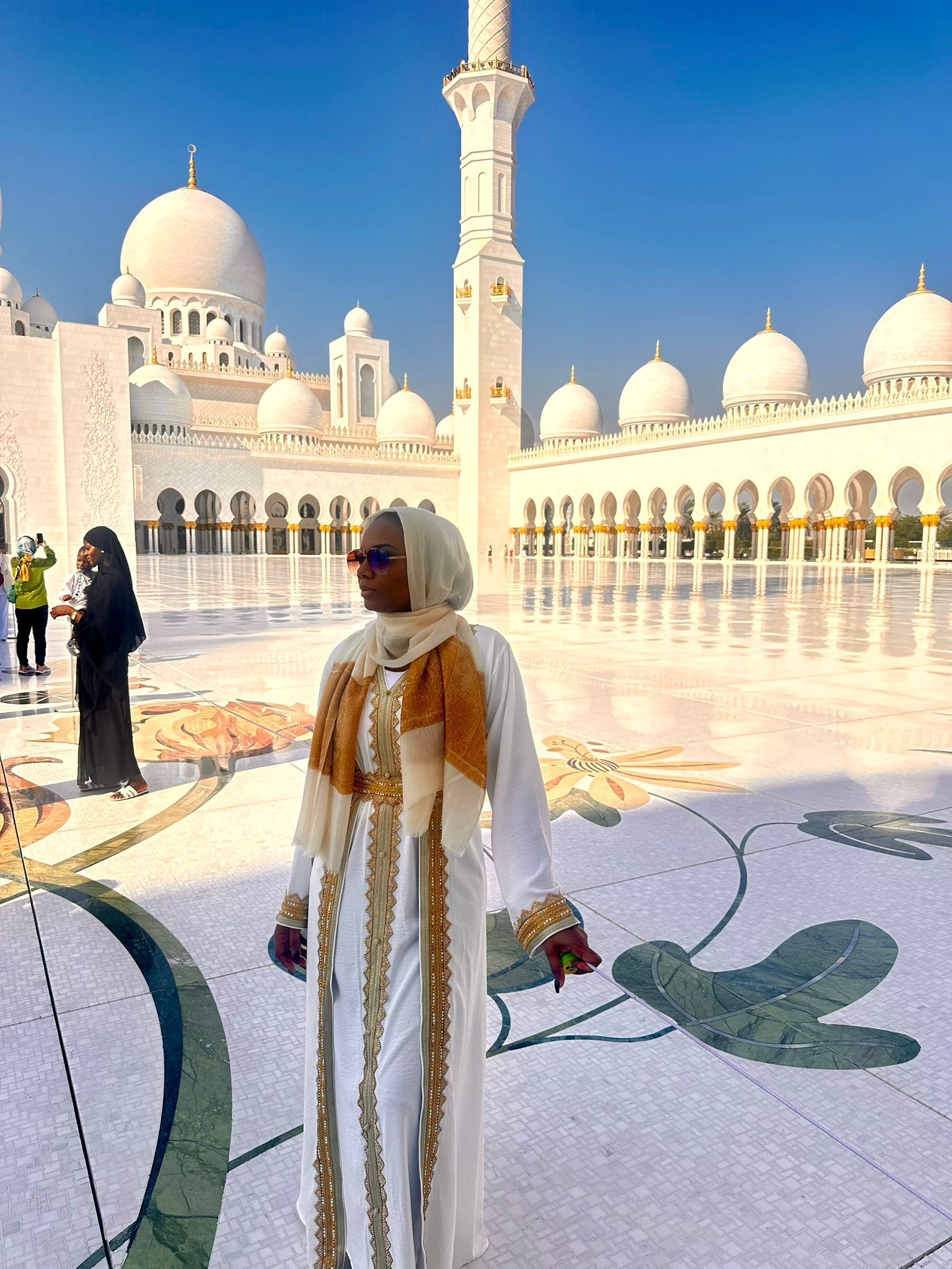 Woman in white robes at the Sheikh Zayed Grand Mosque in Abu Dhabi, sunny day.