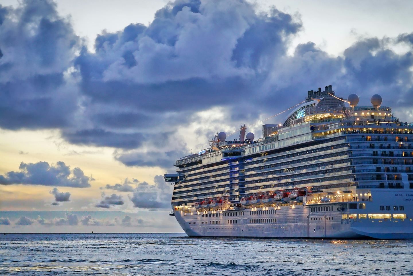 A large cruise ship traveling towards the horizon with clouds seen in the distance