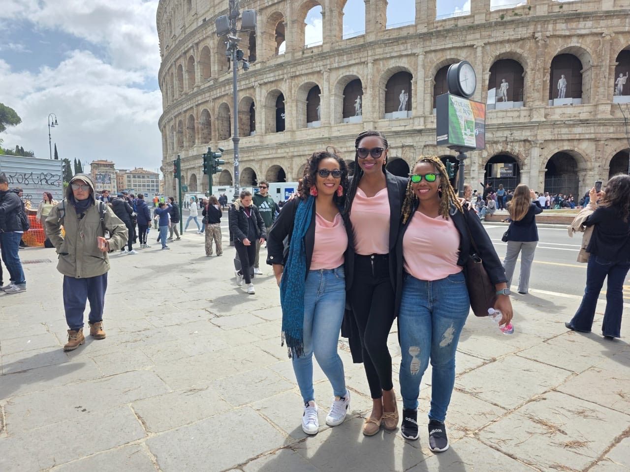 Three people posing in front of the Colosseum in Rome. People and buildings are in the background, sunny day.