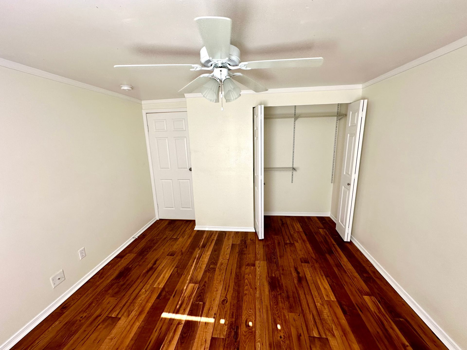 Empty bedroom with hardwood floors, closet, and a white ceiling fan.