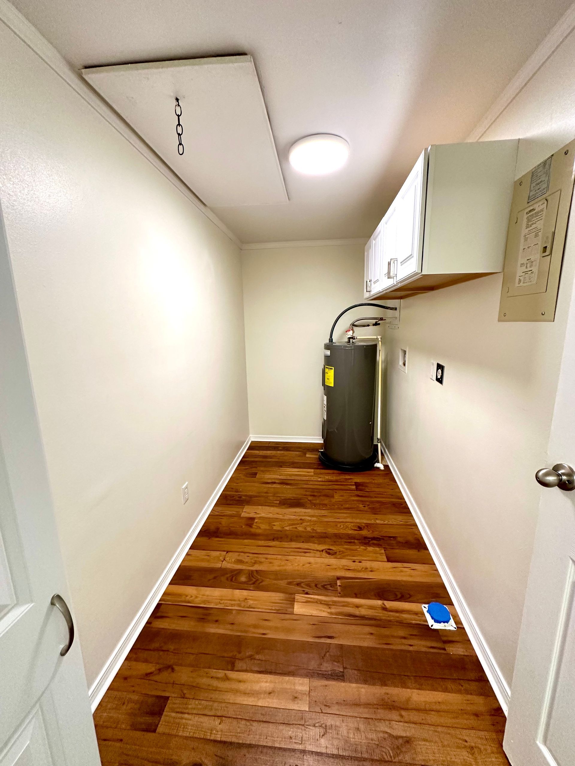 Small laundry room with wood floor, water heater, and a hanging attic access.