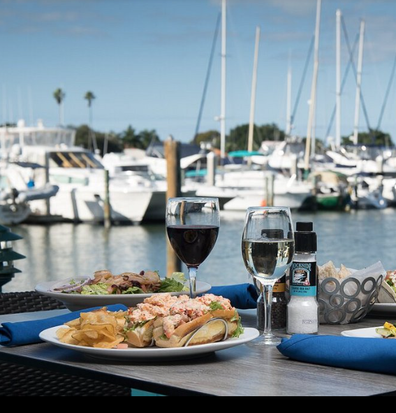 Table with seafood meal and wine overlooking a marina with boats.