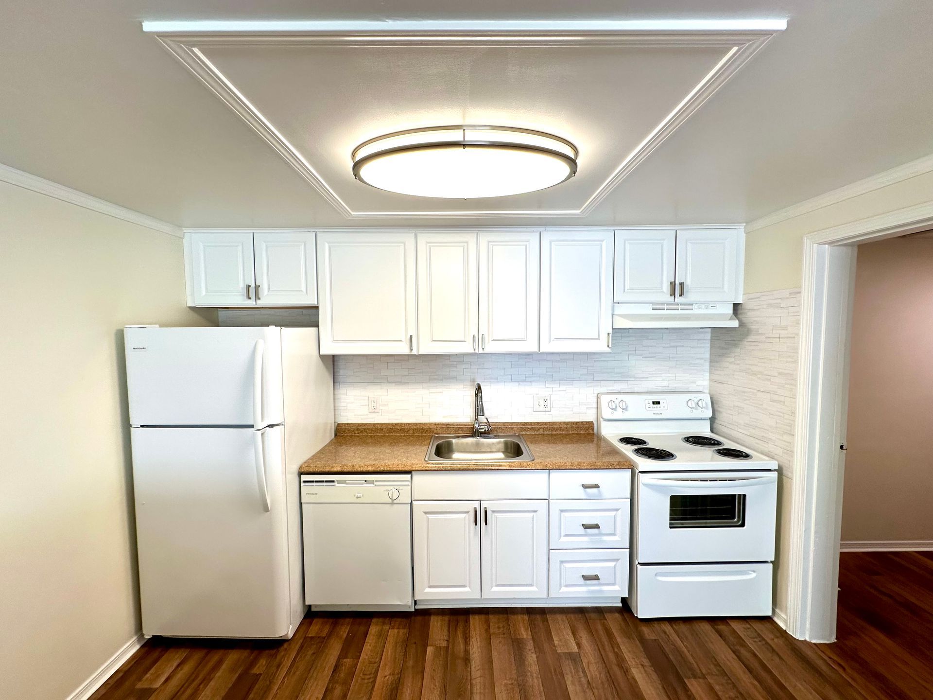 White kitchen with appliances, cabinets, and a sink. Wooden floor and beige backsplash.