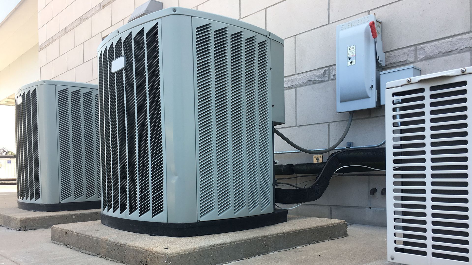Two air conditioners are sitting on the side of a building.