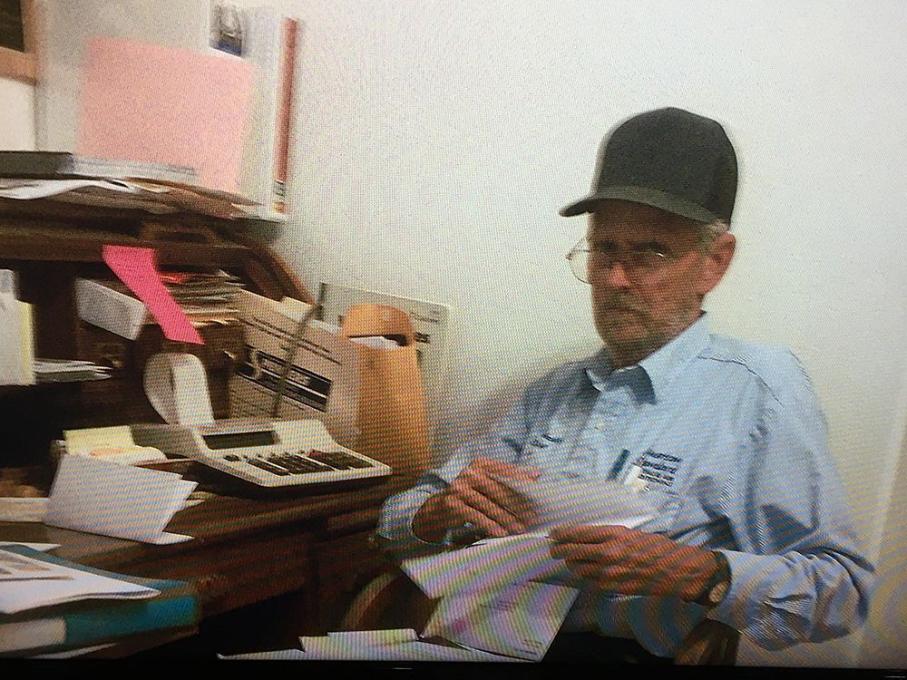 An older man is sitting at a desk holding a piece of paper.