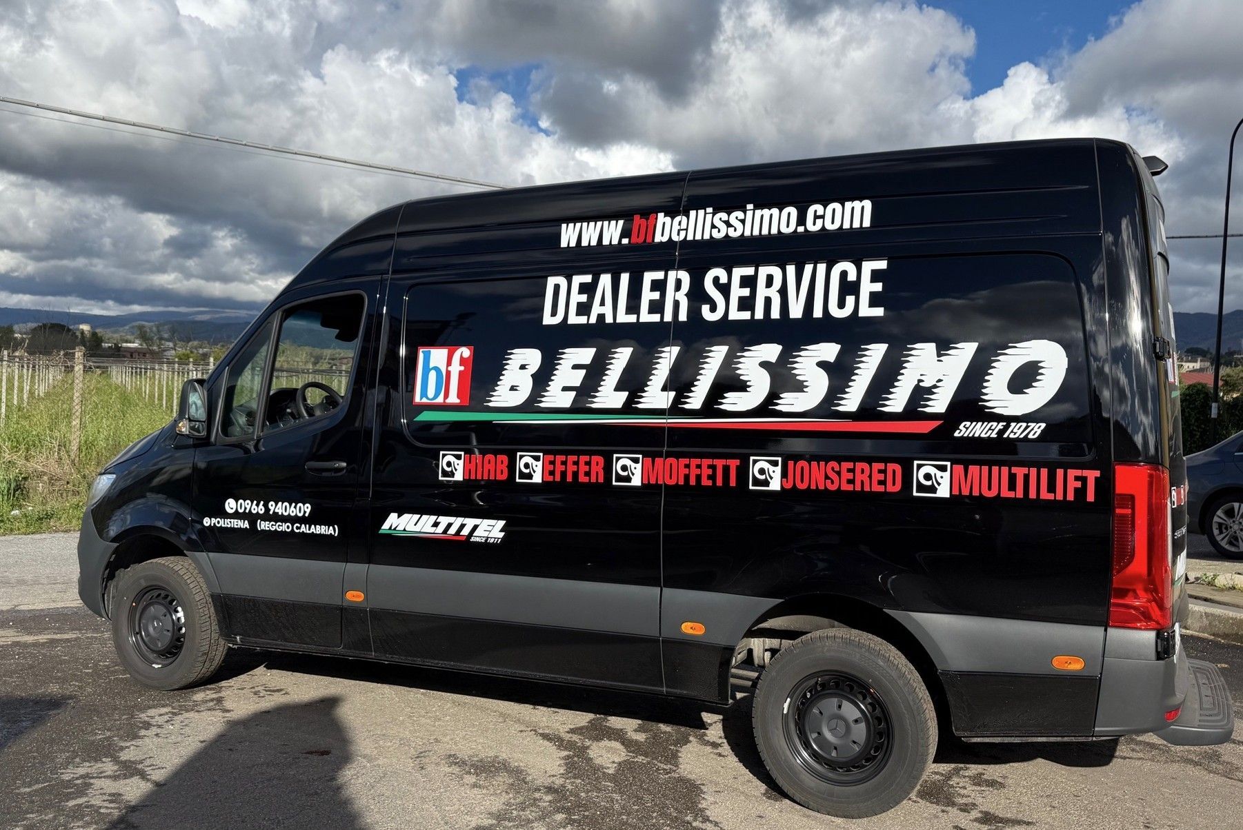 A black van with the words dealer service bellissimo on the side is parked in a parking lot.