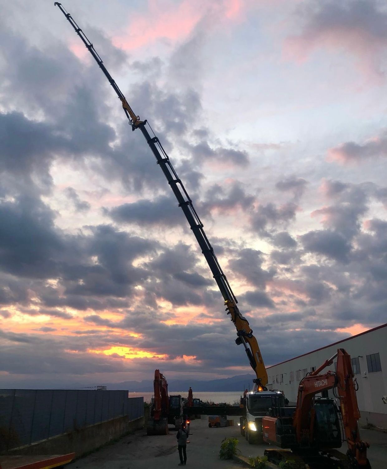 A crane with a very long arm is in a parking lot at sunset