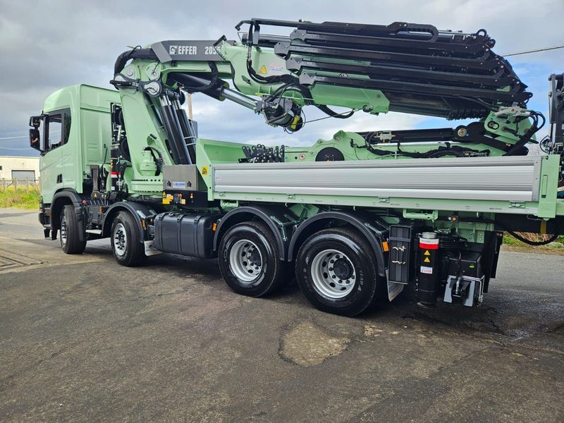 A green truck with a crane on the back is parked on the side of the road.