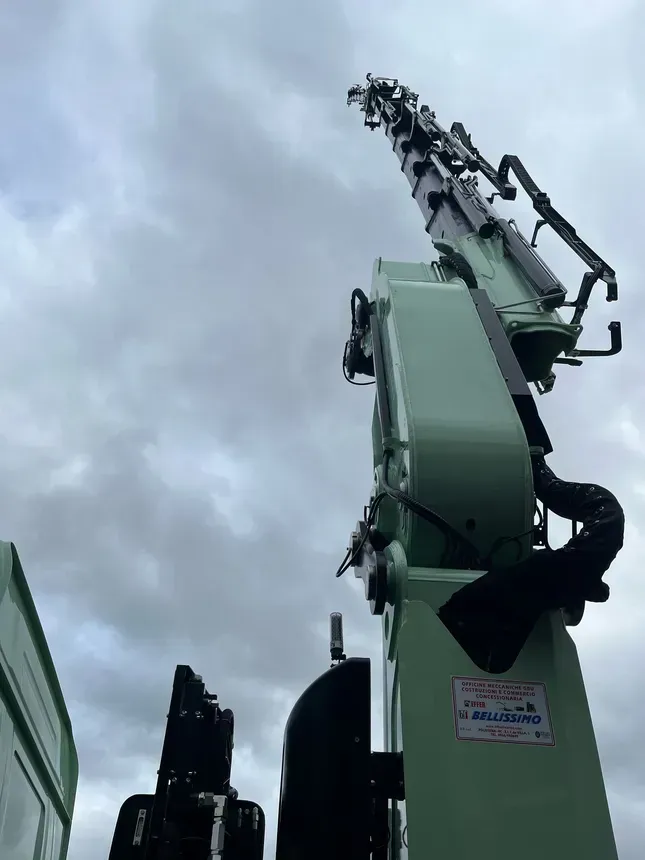 A large green crane is sitting in front of a cloudy sky.