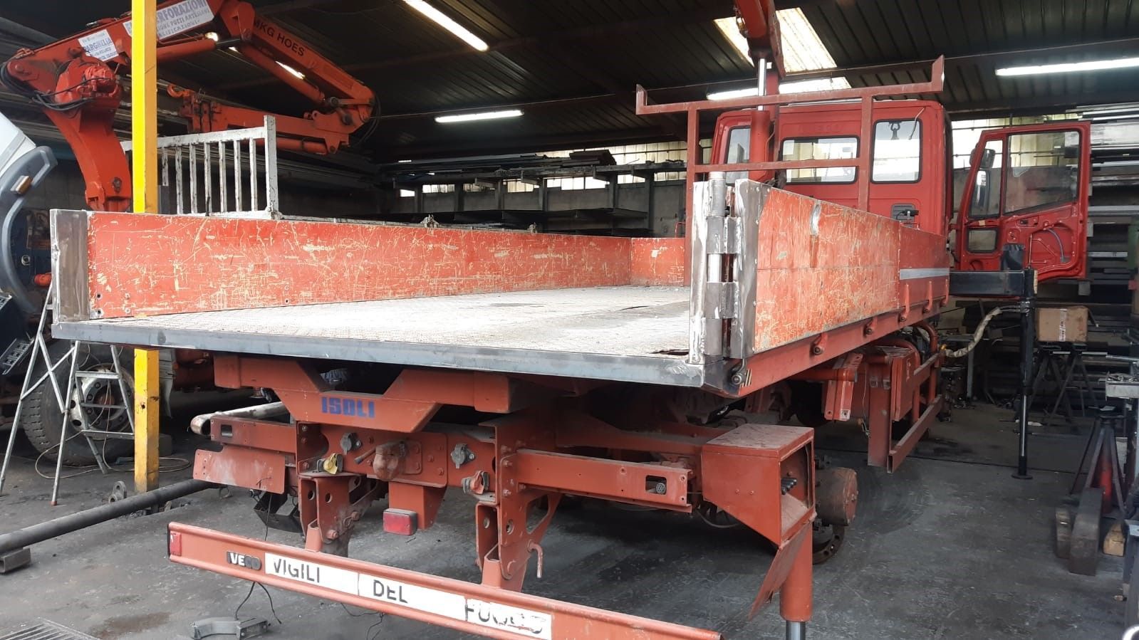 A red truck with a flat bed is parked in a garage.