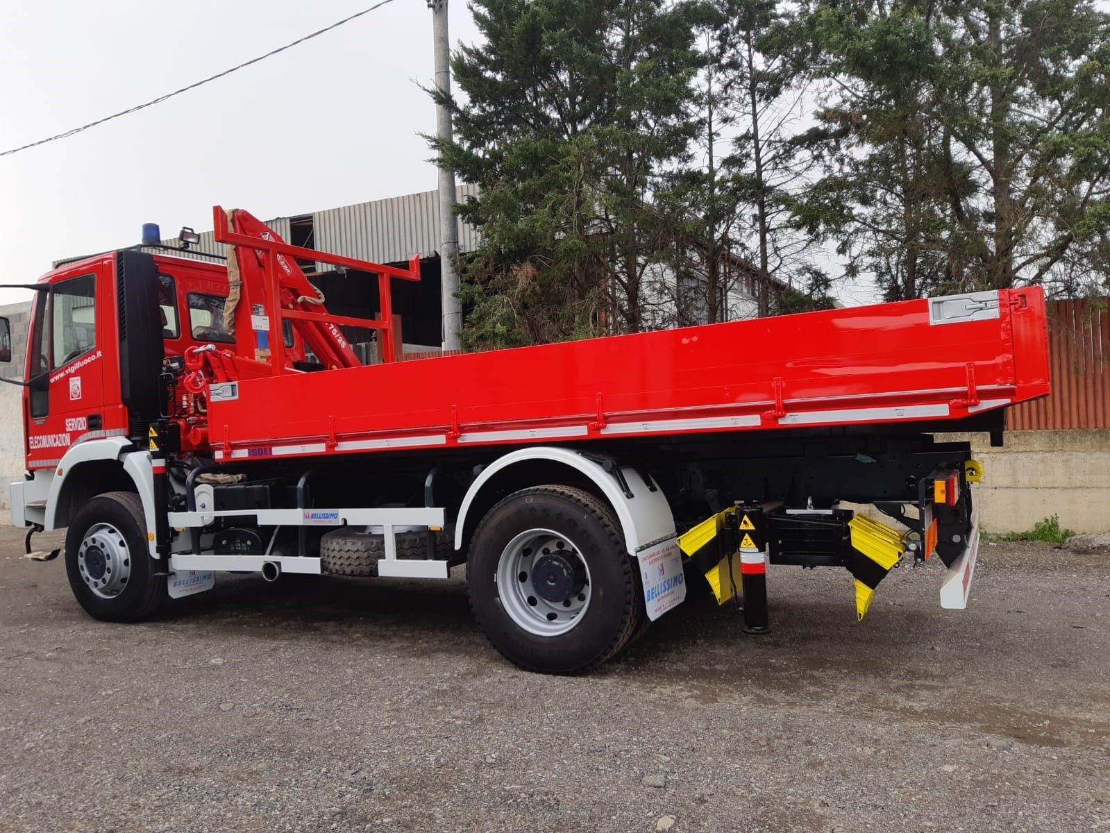 A red truck with a crane on the back is parked in a gravel lot.