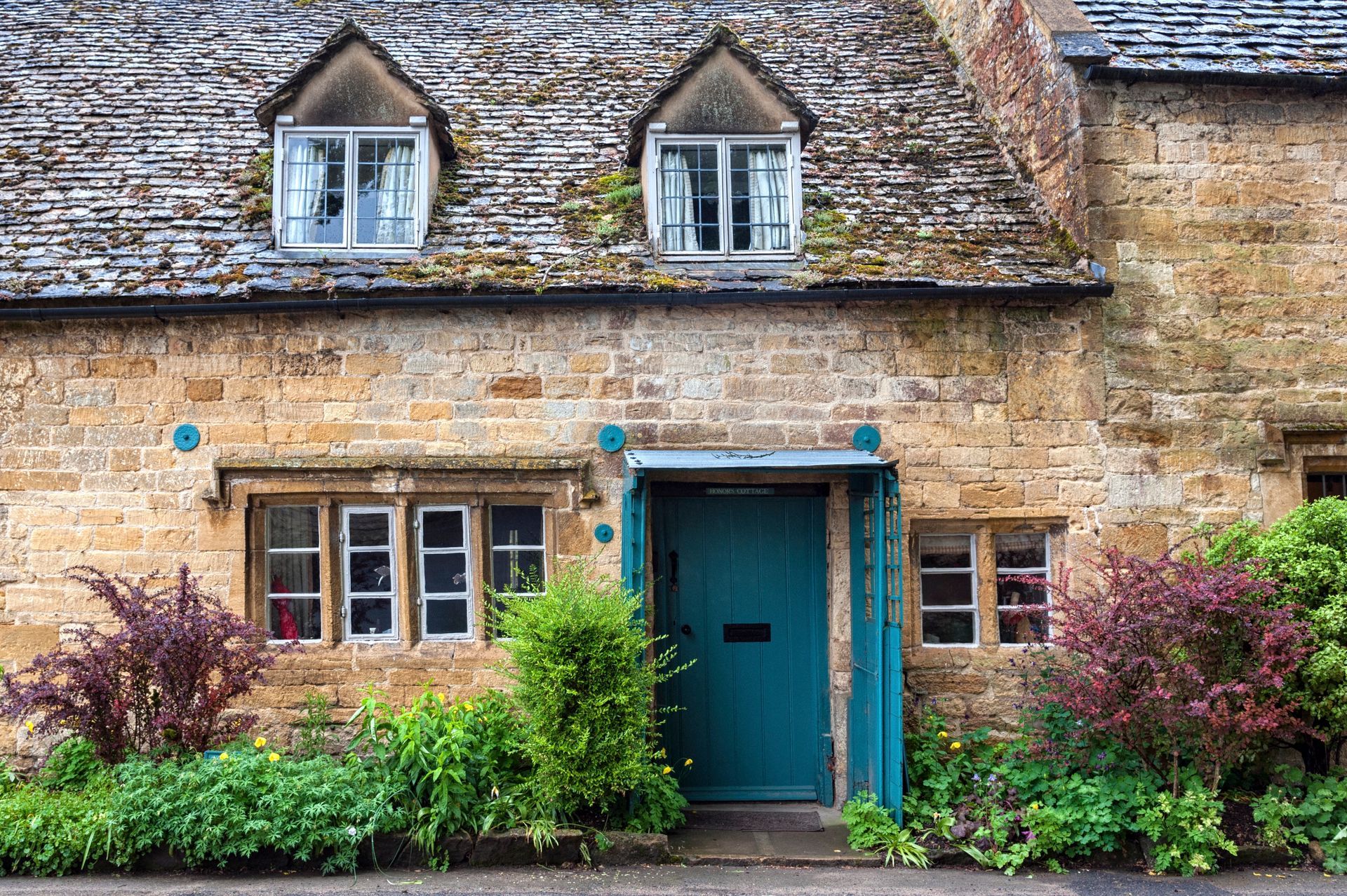 Quaint blue front door to traditional stone cottage inSnowshill, The Cotswold's Gloucestershire, England, with poor guttering system to front roof.