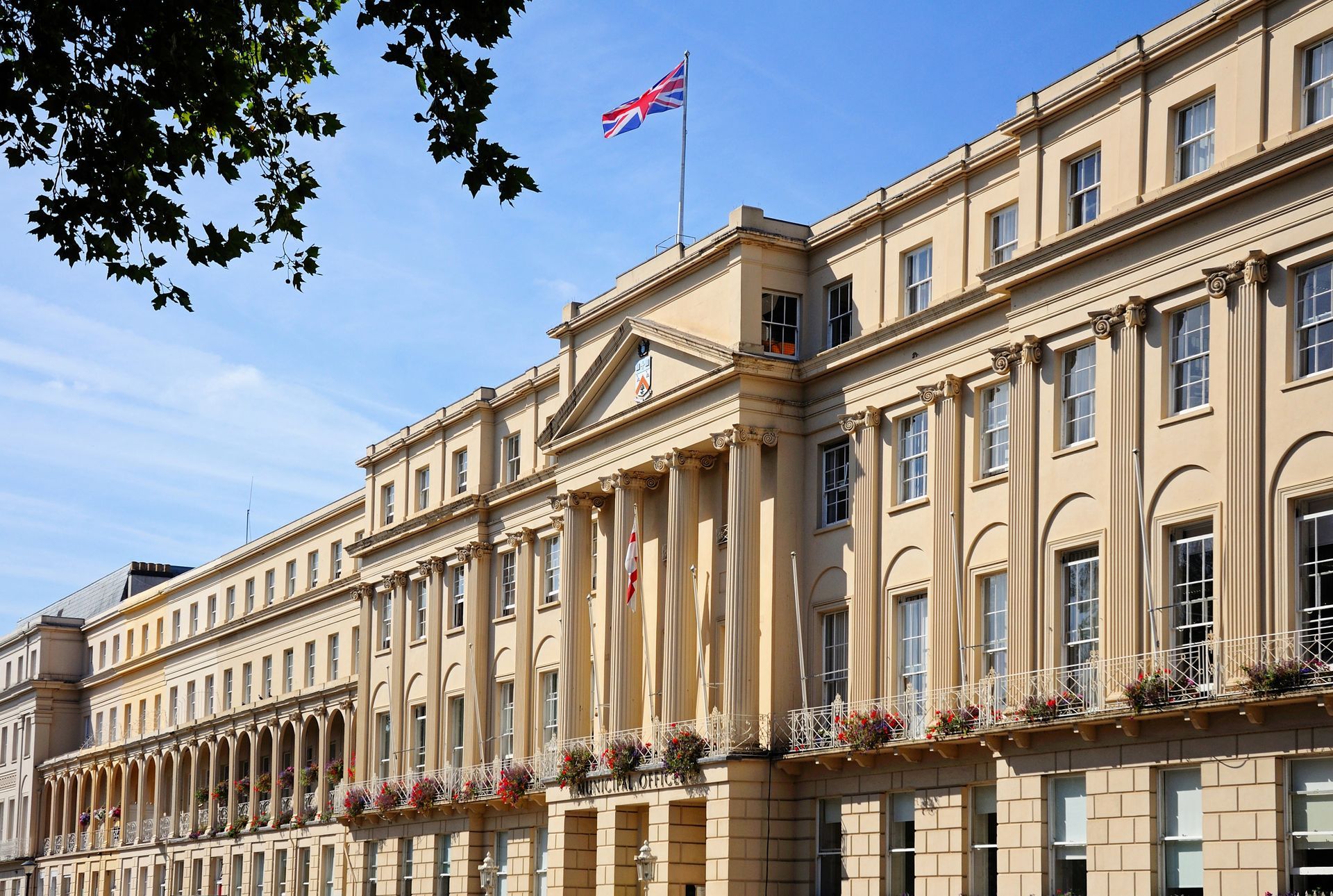 A view along the front of the Council Municipal buildings on the Promenade at Cheltenham Spa, Gloucestershire, United Kingdom, with a Union Flag flying on top of the building.