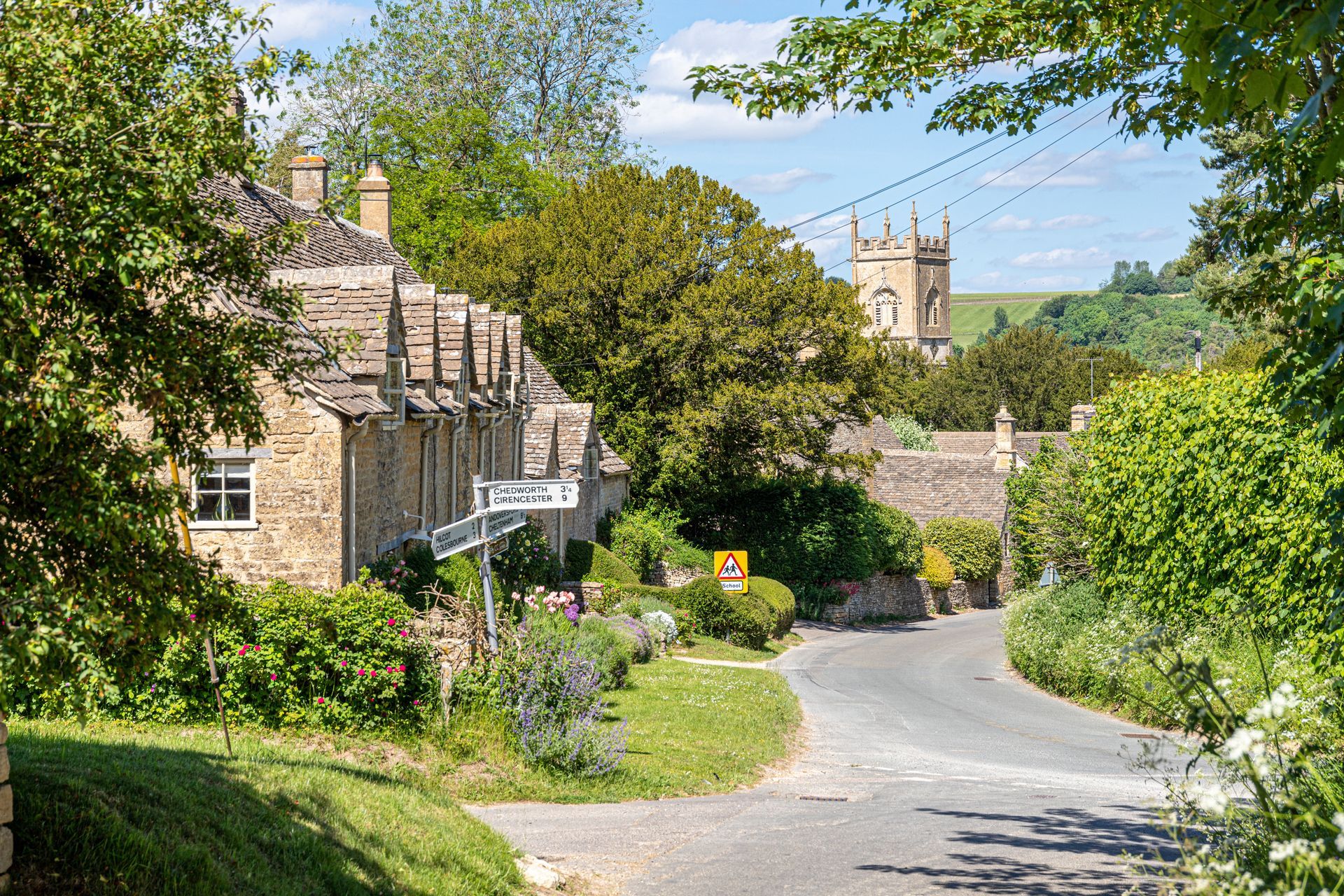 The Cotswold village of Withington, Gloucestershire, United Kingdom. The view is looking down a street on a hill past some historic Cotswold houses towards a Norman Church in the distance.