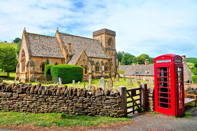 an image of a traditional english church in the Cotswolds with a red british telecomms phone box in the foreground.