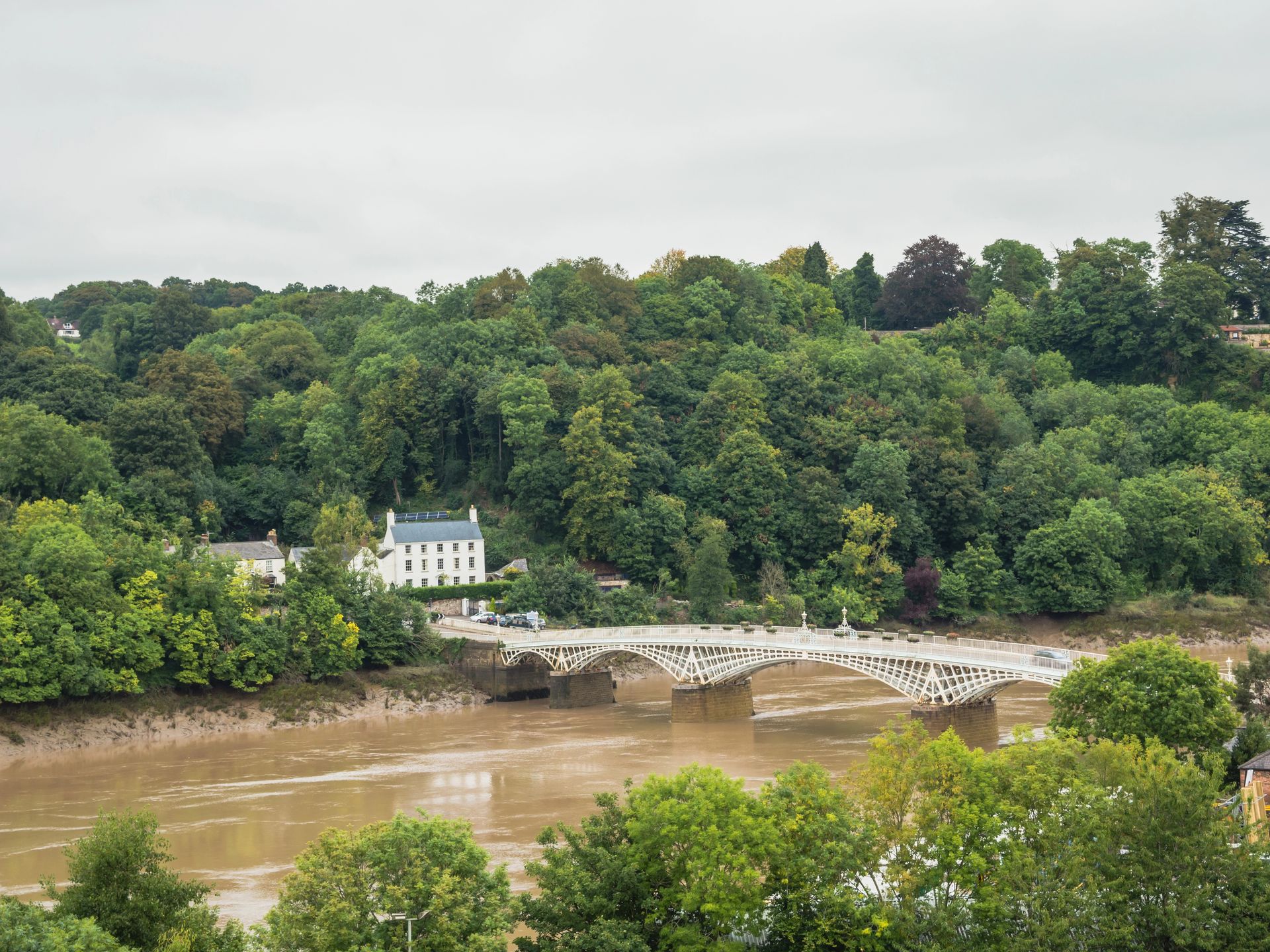 View from Chepstow, Monmouthshire in Wales across the River Wye to a Georgian white house on the English side of the River Wye in Gloucestershire, with a historic white road bridge extending over the River Wye.