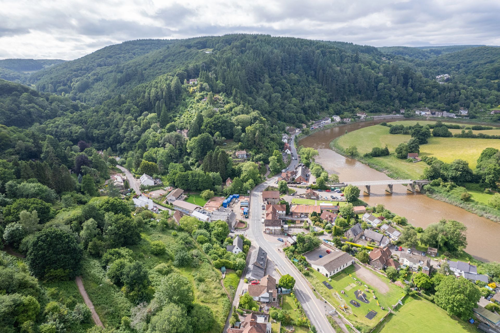 Aerial view of Tintern, Monmouthshire nestled in a green valley beside the River Wye with a bridge over to England.