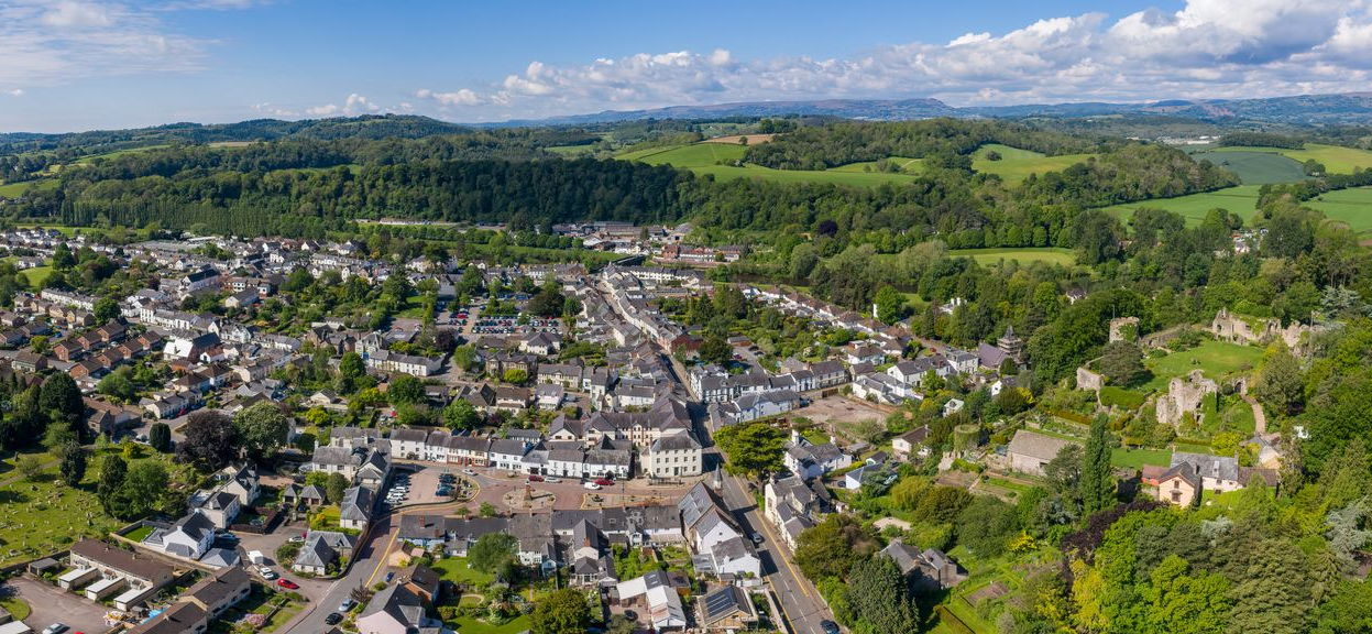 Ariel view of the town of Usk, Monmouthshire overlooking the town square towards the River Usk in the far background. Usk Castle sits to the right of the image on a hill overlooking the town.