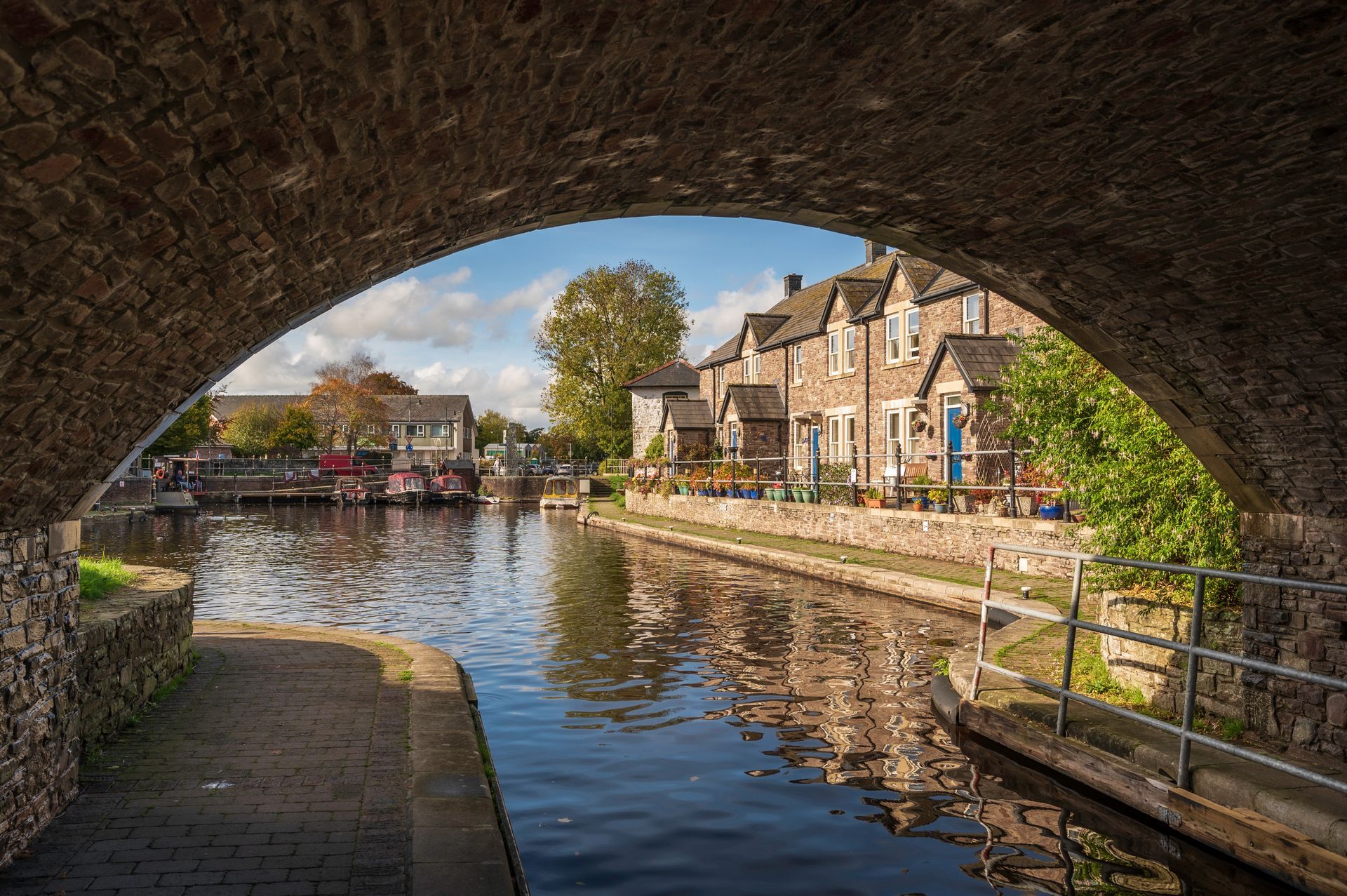 View of pretty canal cottages from beneath a canal bridge on the Brecon - Monmouthshire Canal near Brecon, Powys, Wales. The sky is blue and the water reflects the scene.
