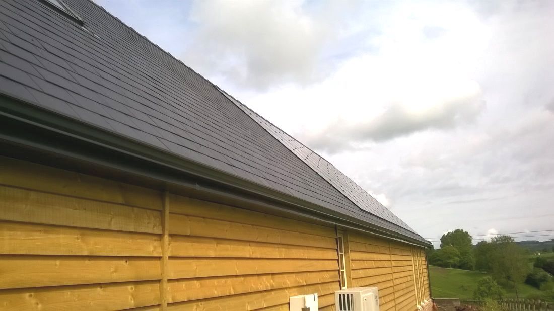 an image of a wooden building with dark grey slate roof with a curved radius gutter system.