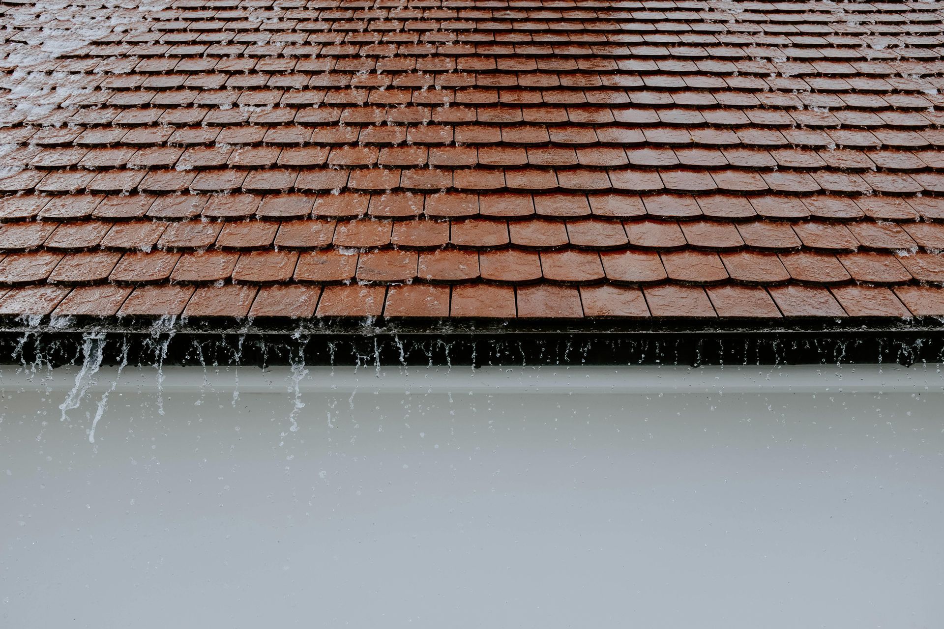 Heavy rain pouring off a brown slate roof into a seamless aluminium gutter system