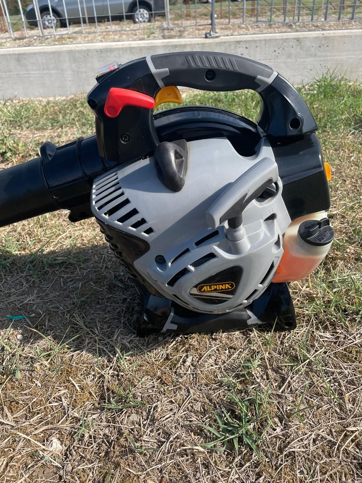 Un soffiatore per foglie nero e grigio su erba secca; una leva rossa in cima.