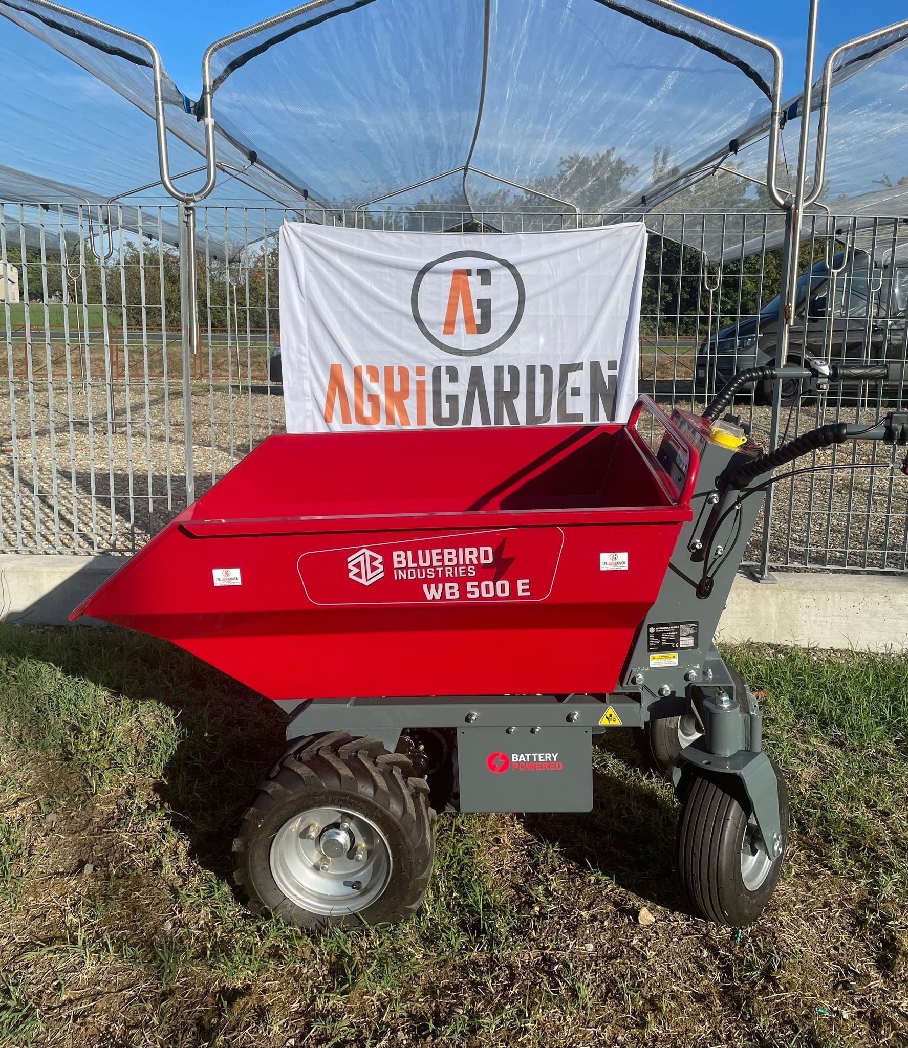 Carriola motorizzata rossa e grigia in un giardino, con uno striscione con la scritta 