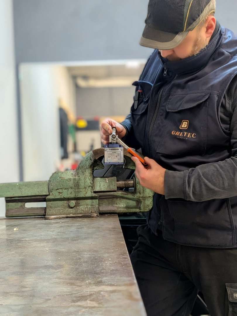 Een persoon in werkkleding gebruikt een metalen stempel en hamer op een stuk metaal dat in een bankschroef is geklemd.