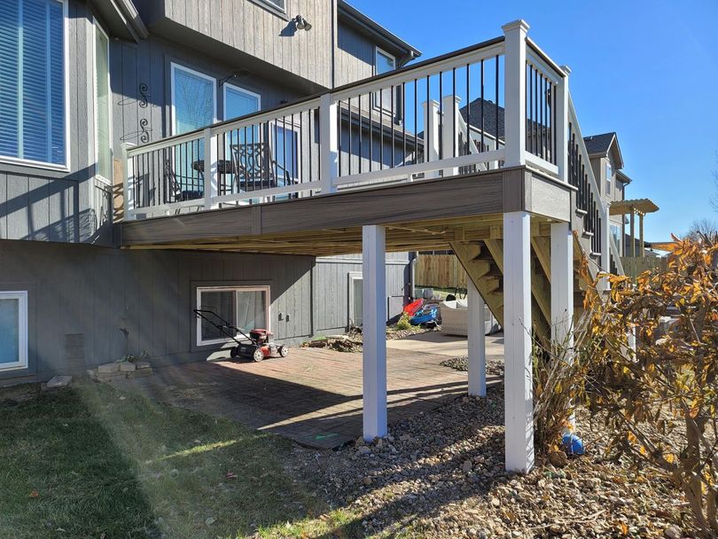 A large deck with stairs leading up to it is in the backyard of a house.