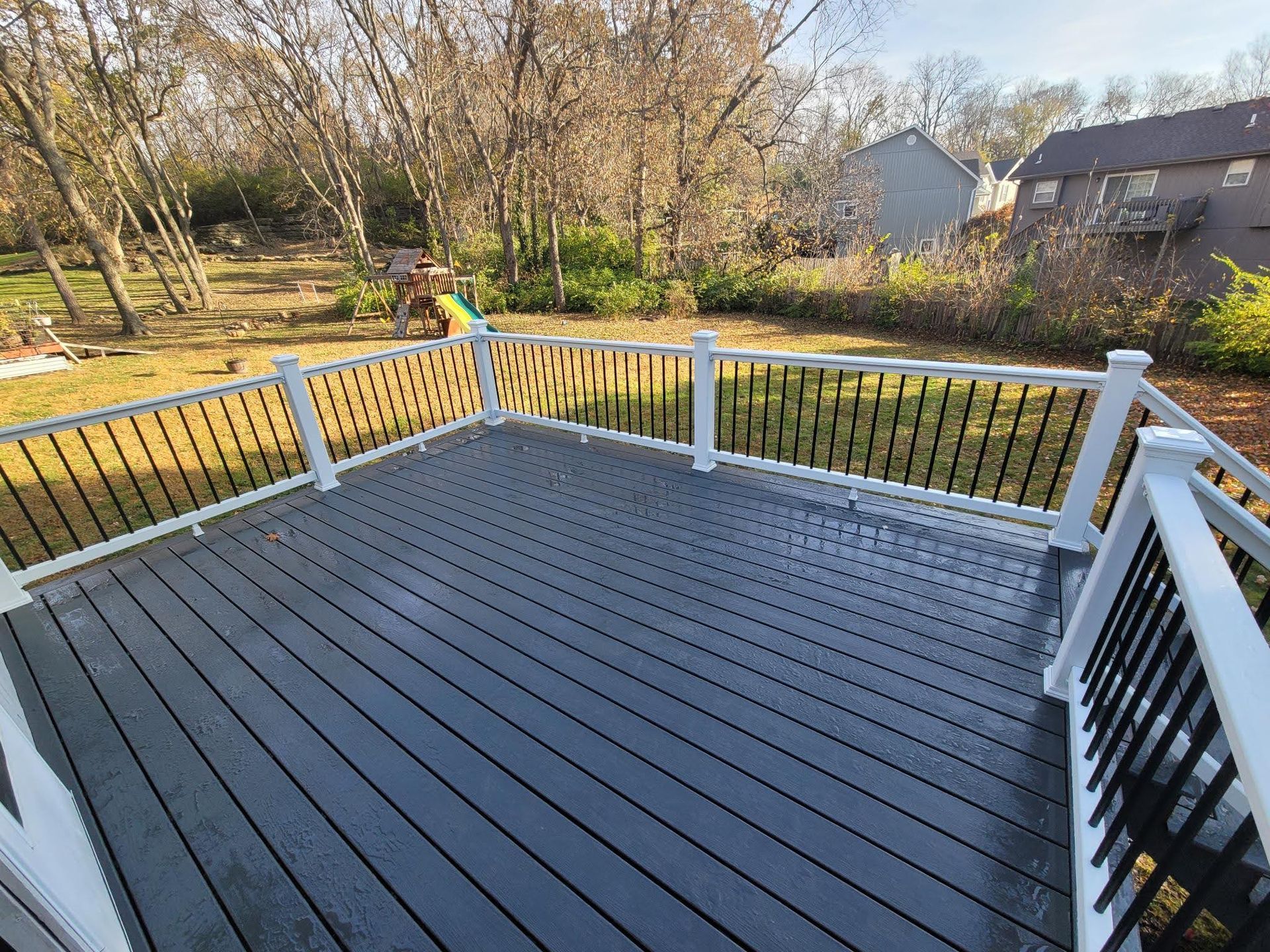 A gray deck with a white railing and a playground in the background.