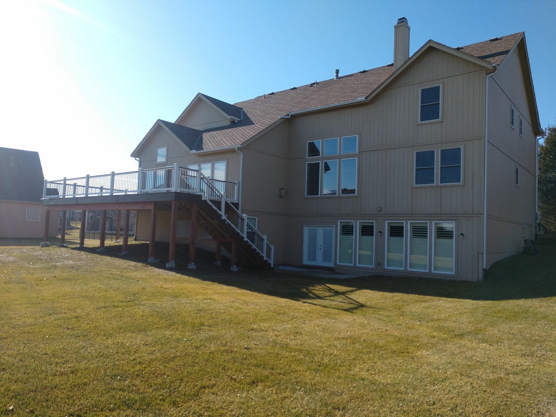 The back of a large house with a large deck and stairs.