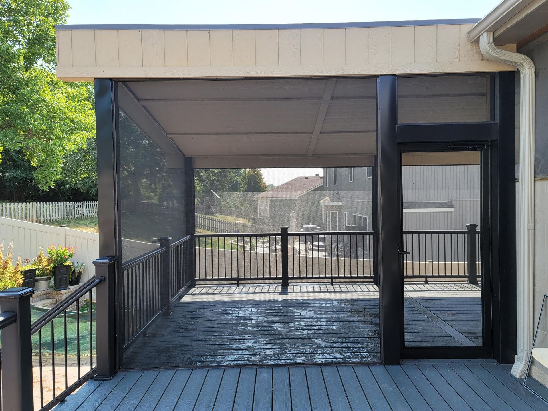 A screened in porch with a black railing and a glass door.