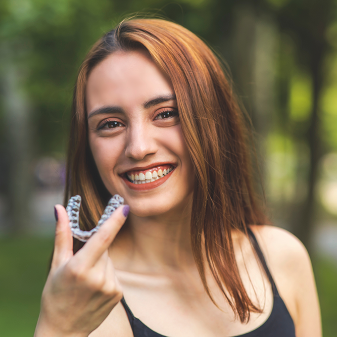 A woman is smiling while holding a clear retainer in her hand.