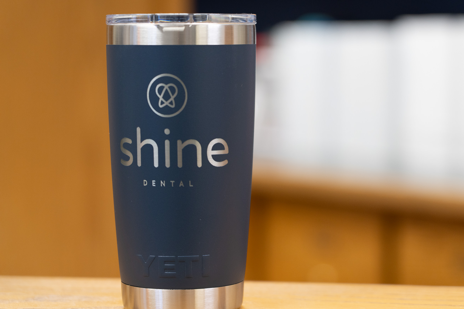 A stainless steel cup with the word shine on it is sitting on a wooden table.
