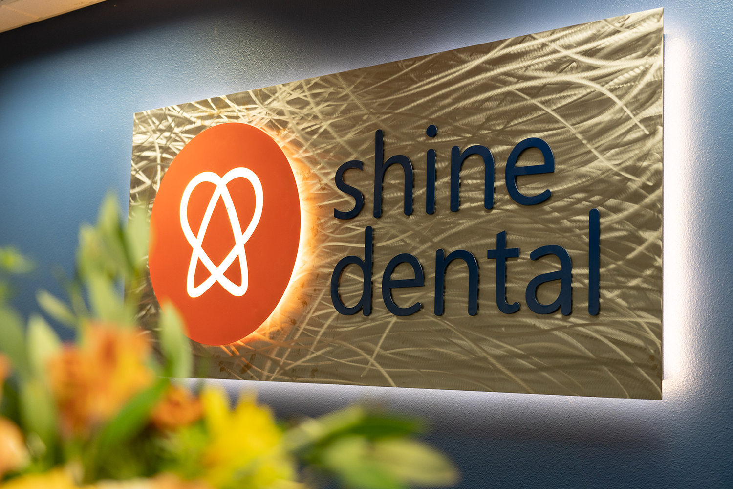 A sign for shine dental is hanging on a wall.
